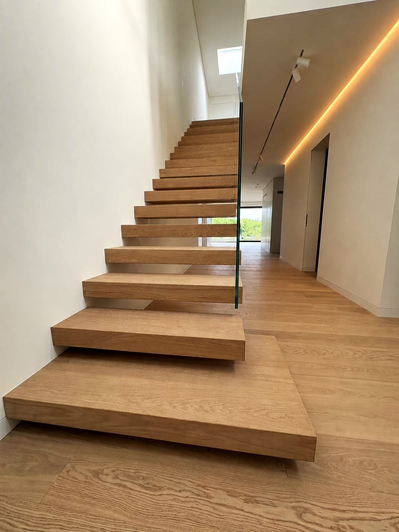 Kragarmtreppe in Eiche vom Antritt aus: Stufen frei aus der Wand, rahmenloses Klarglasgeländer an der offenen Seite