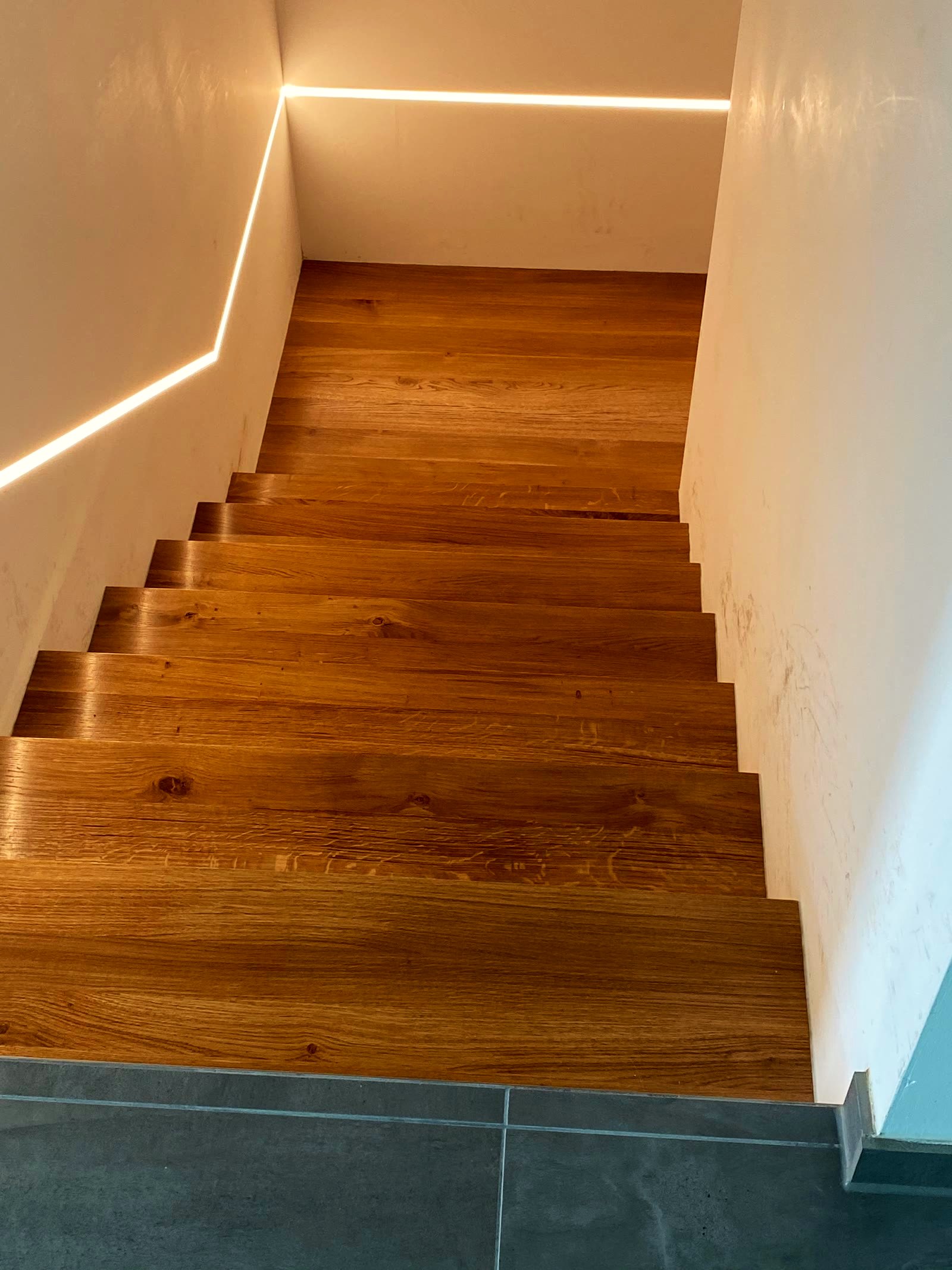 Dieselbe Treppe von unten, die Lichtlinie folgt dem Treppenlauf über zwei Wände