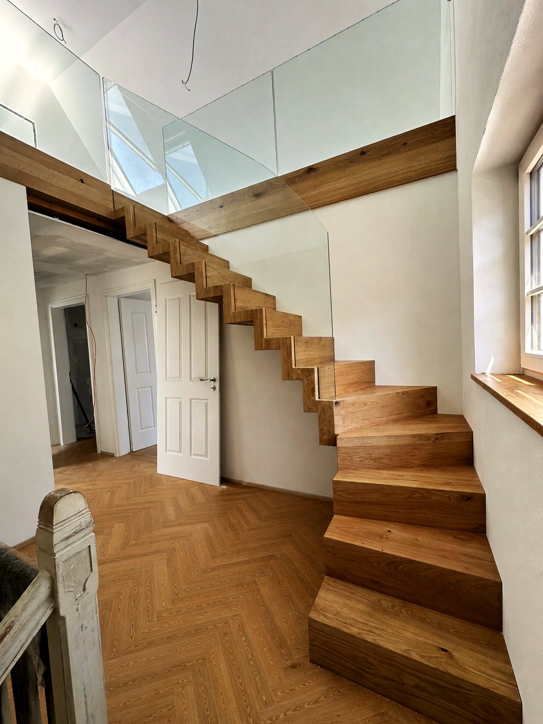 Faltwerktreppe aus Eiche in einem Altbau mit Fischgrätparkett, oben die Galerie mit Glasgeländer
