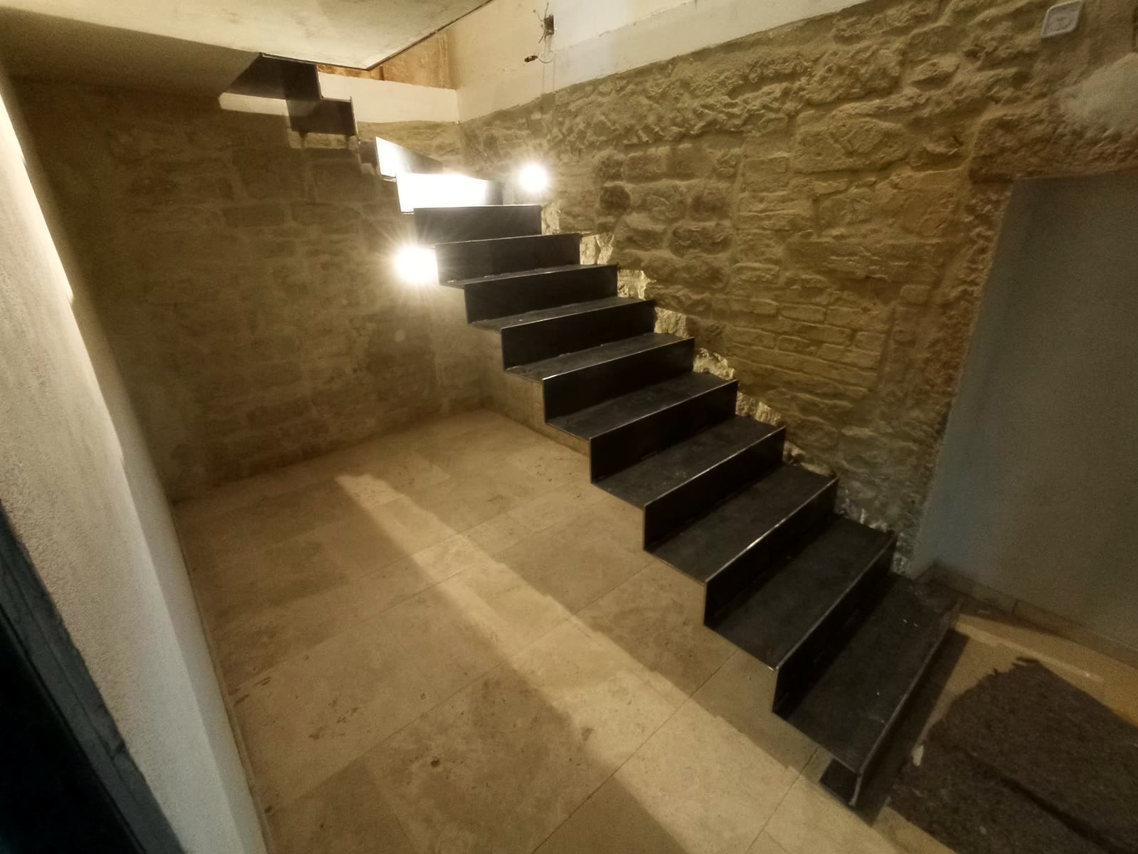 Stahl-Faltwerktreppe im Rohzustand vor einer Bruchsteinwand, Stufenleuchten bereits eingebaut